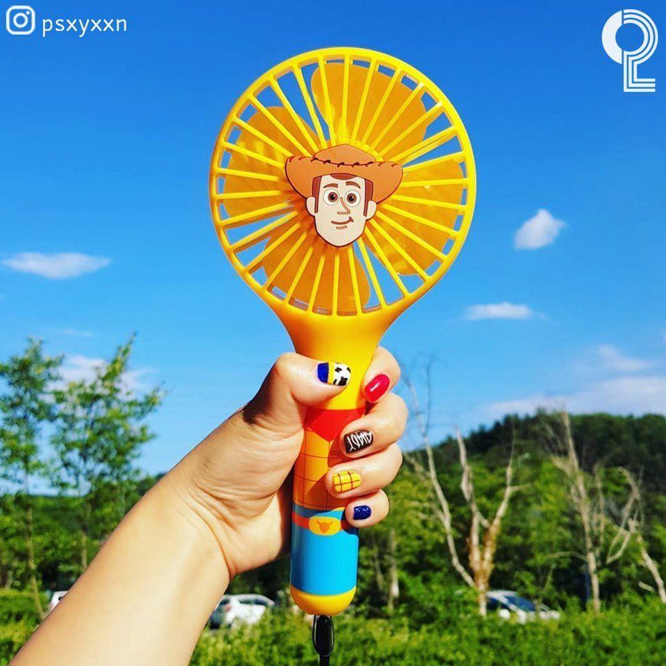 夏日户外使用的黄色胡迪电风扇，手握视角展示，背景为蓝天与绿树。